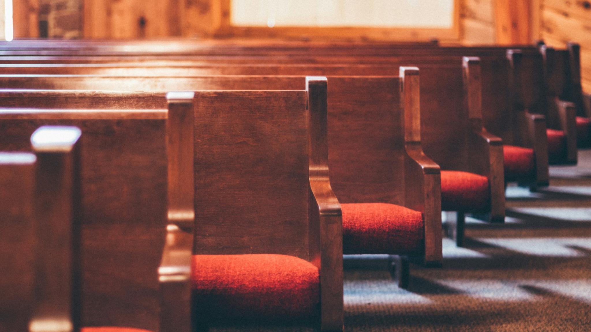 Man sieht einige Reihen mit Kirchenbänken, die rote Polster auf der Sitzfläche haben