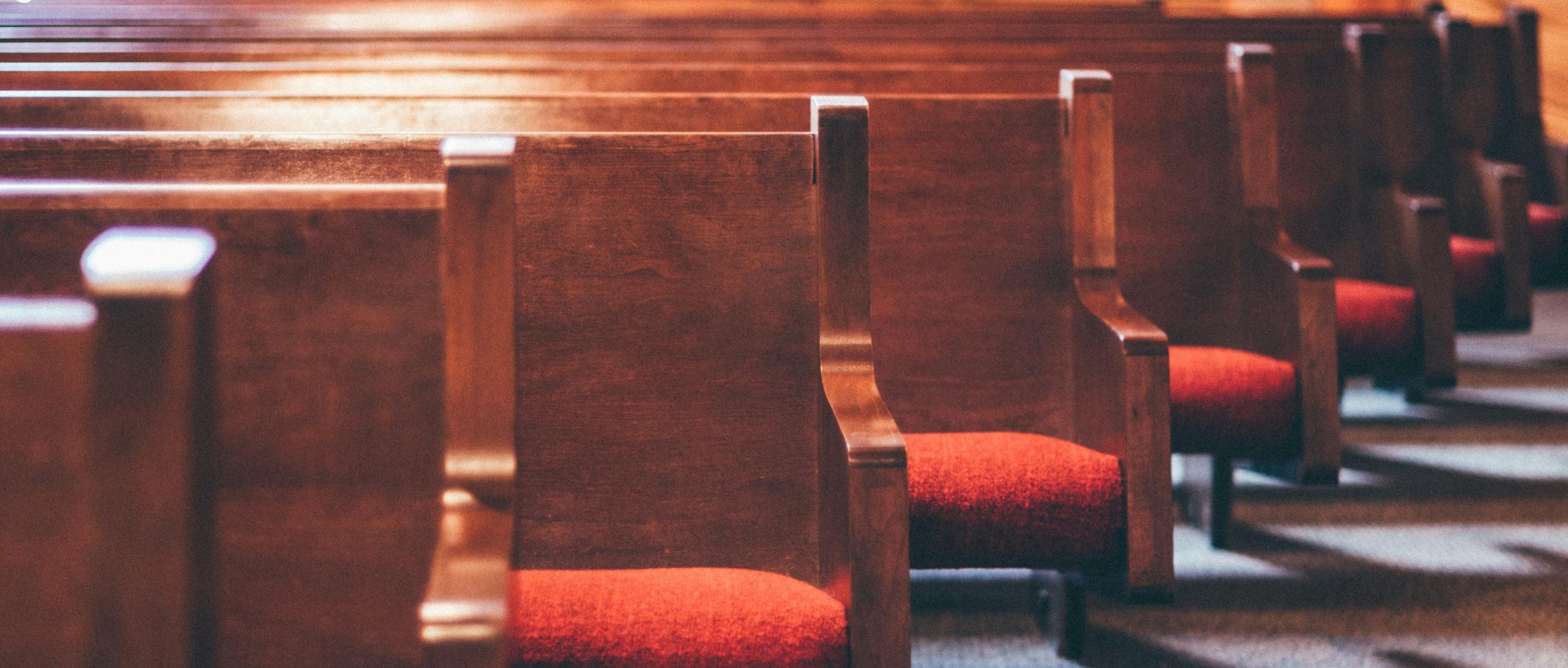 Man sieht einige Reihen mit Kirchenbänken, die rote Polster auf der Sitzfläche haben